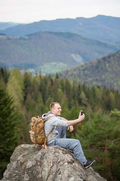 Alpinista masculino com mochila marrom no pico da rocha — Fotografia de Stock
