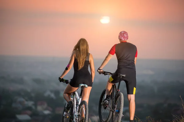 Couple bicyclist with mountain bikes on the hill at sunset — Stock Photo, Image