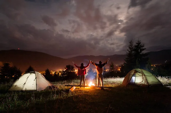 Acampamento nocturno. Par de turistas de pé e de mãos erguidas — Fotografia de Stock