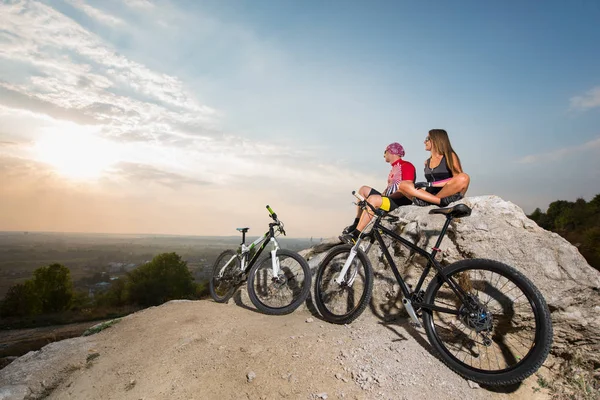 Glückliches Radlerpaar mit Sonnenbrille auf einem Felsen sitzend — Stockfoto