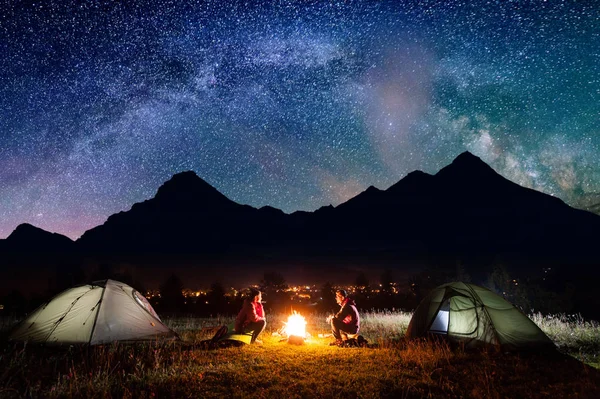 Man och kvinna som sitter nära tält på kvällen — Stockfoto