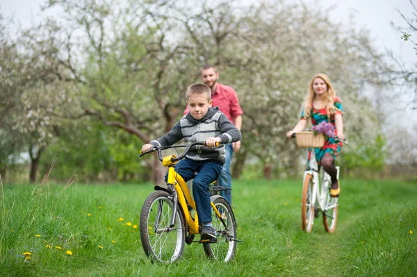 Familia feliz en una bicicleta en el jardín de primavera — Foto de Stock