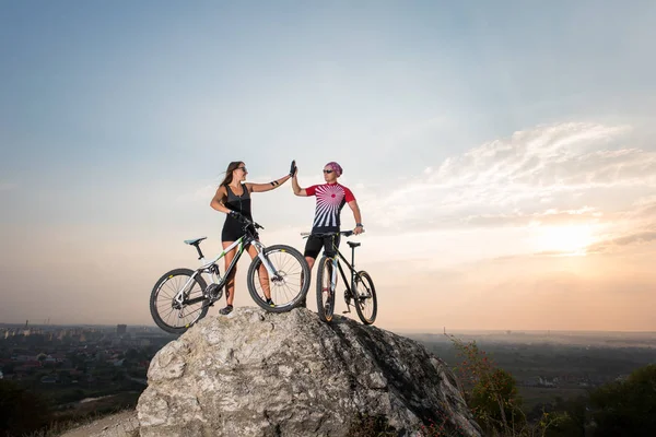 Couple standing with bicycles on the rock under evening sky