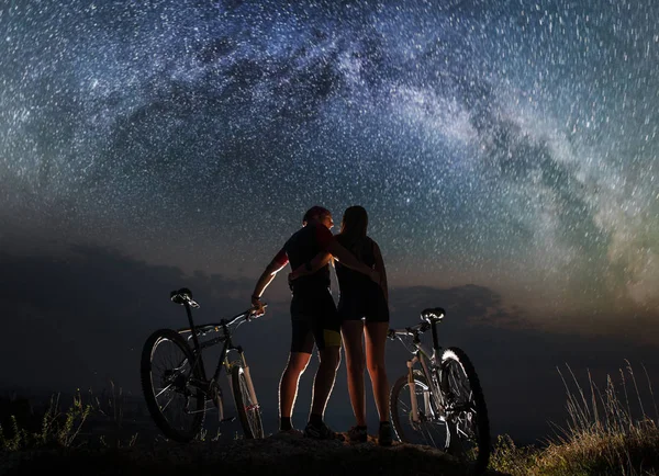 Couple cyclists with mountain bikes at night under starry sky — Stock Photo, Image