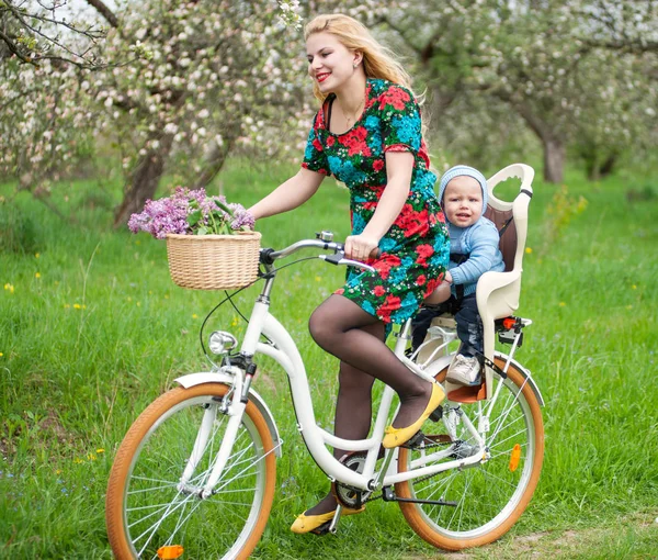 Bionda donna in sella alla città in bicicletta con bambino in sedia a rotelle — Foto Stock