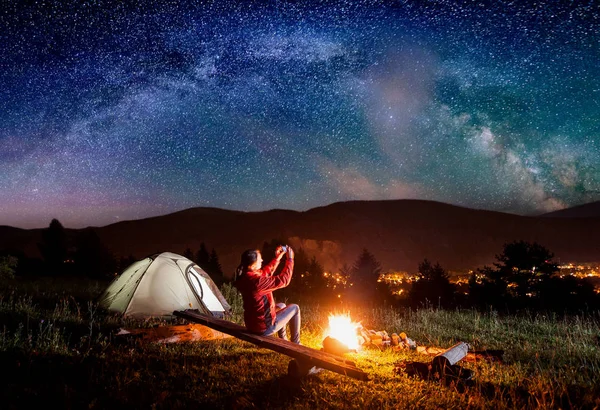 Wanderin sitzt auf Brettern am Lagerfeuer in der Nähe von Zelt und macht — Stockfoto