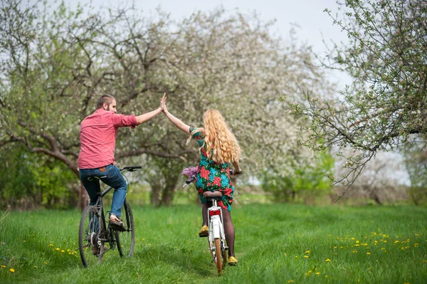 Amar pareja joven montar en bicicleta en el jardín de primavera — Foto de Stock