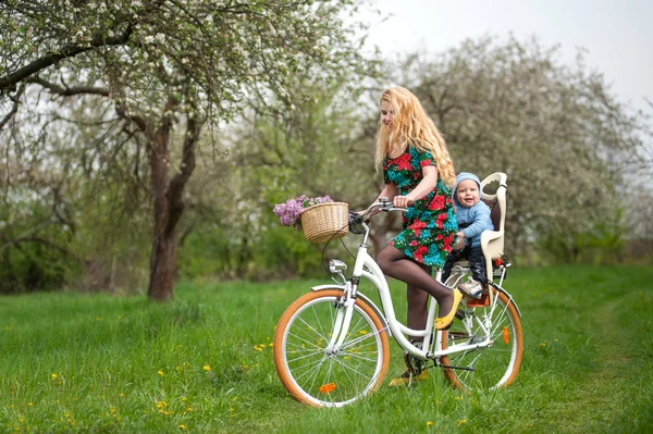 Blondynka konna kobiece miasto rowerów z dzieckiem w fotelu rowerów — Zdjęcie stockowe