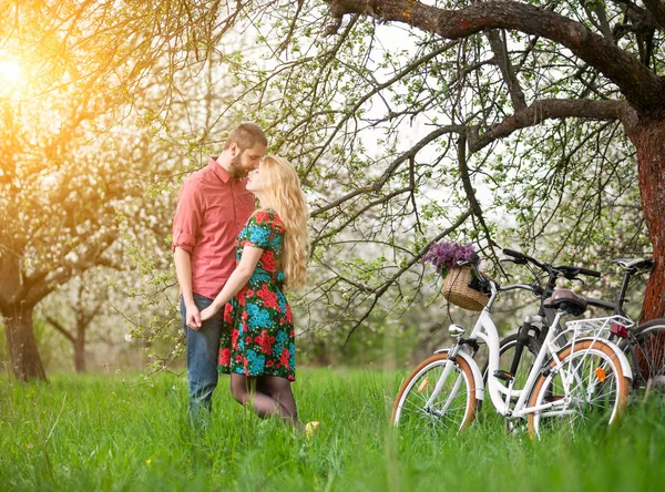 Amantes pareja joven con bicicletas en el jardín de primavera —  Fotos de Stock