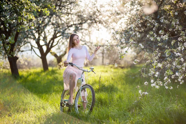 Hermosa ciclista femenina con bicicleta retro en el jardín de primavera — Foto de Stock