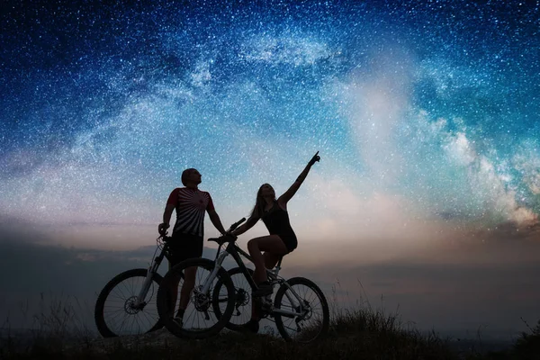 Couple cyclists with mountain bikes at night under starry sky — Stock Photo, Image