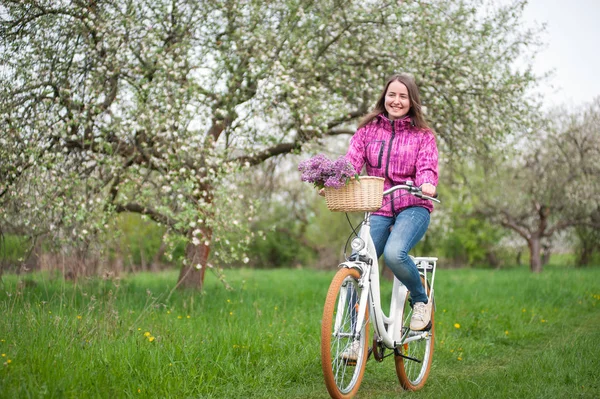 Mujer ciclista montando una bicicleta blanca vintage en el jardín de primavera — Foto de Stock