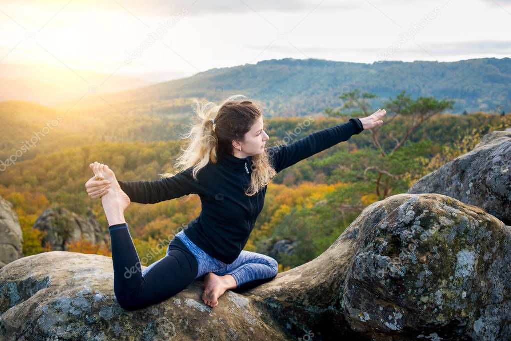Sporty fit woman is practicing yoga on the top of the mountain