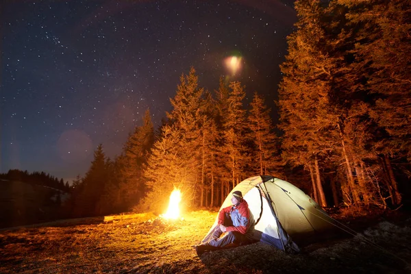 Człowiek siedzi w pobliżu ogniska i namiot — Zdjęcie stockowe