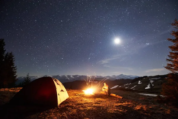 Kamp ateşi ve çadır yakınında oturan adam