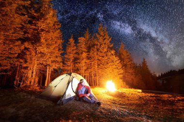 Kamp ateşi ve çadır yakınında oturan adam