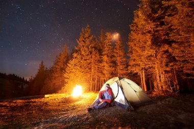 Kamp ateşi ve çadır yakınında oturan adam