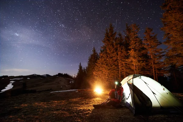 Kamp ateşi ve çadır yakınında oturan adam