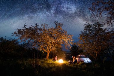 Bir kamp ateşi oturan üç turist 