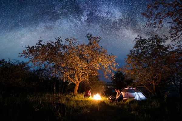 Bir kamp ateşi oturan üç turist 