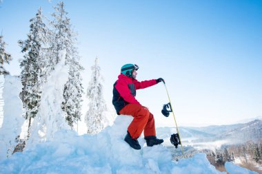  karlı bir tepenin üstüne oturan snowboarder 