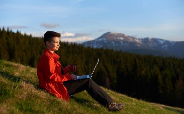 Dışarıda dizüstü bilgisayar kullanan genç bir kadın.
