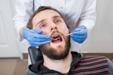 Sakallı adamın diş onay diş ofiste olan kadar yakın. Dişçi bir hastanın diş diş araçları - ayna ve sonda ile incelenmesi. Diş Hekimliği.