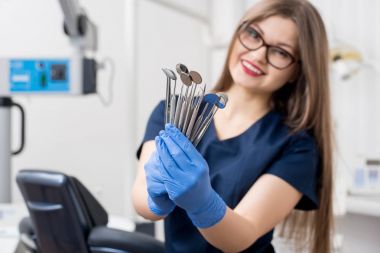 Mavi eldiven araçları - diş aynalar ve diş ofiste diş sondalar holding ile gülümseyen kadın dişçi. Yakın çekim, seçici odak üstünde alet. Diş Hekimliği