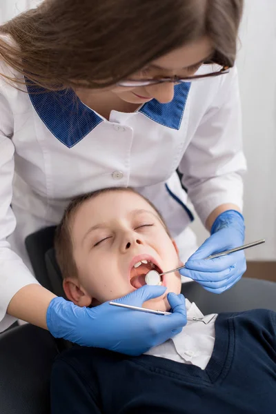 La dentista femenina examina los dientes del niño paciente. La boca del niño se abre de par en par en la silla del dentista. Primer plano — Foto de Stock