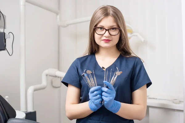 Genç kadın çekici dişçi diş araçları - aynalar ve sondalar morden diş ofiste tutan portresi. Gözlük, mavi üniforma, eldivenler ve kameraya bakarak doktor. Diş Hekimliği — Stok fotoğraf