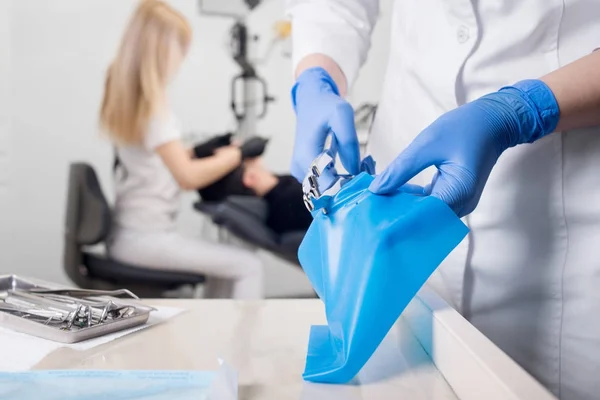 Vista de cerca de las manos del asistente con guantes azules que trabajan con el dispositivo dental, en el fondo borroso dentista está tratando al paciente en la clínica dental. Odontología — Foto de Stock