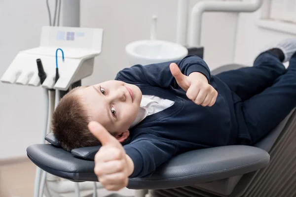 Feliz chico paciente mostrando pulgares en el consultorio de la clínica dental. Medicina, estomatología y concepto de salud. Equipos dentales — Foto de Stock