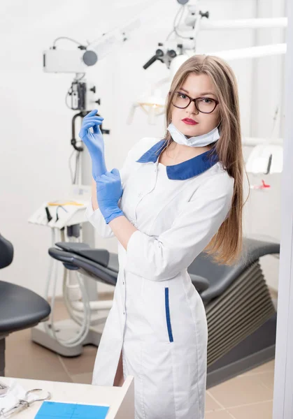 Porträt einer jungen schönen Zahnärztin mit blauen Handschuhen, Brille, Maske, weißer Uniform und Blick in die Kamera in der Morden Zahnarztpraxis. Zahnmedizin — Stockfoto