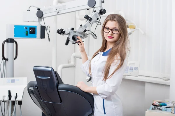 Πορτραίτο του ελκυστική γυναίκα οδοντίατρος με μικροσκόπιο στο οδοντικό γραφείο morden. Γιατρός φοράει γυαλιά, λευκή στολή και αναζητούν στη φωτογραφική μηχανή. Οδοντιατρική — Φωτογραφία Αρχείου