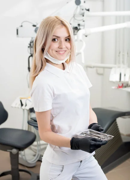 Retrato de una joven y atractiva dentista que sostiene instrumentos dentales en el consultorio dental de Morden. Médico con máscara, guantes negros y mirando a la cámara. Odontología — Foto de Stock