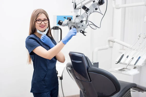 Πορτραίτο του φιλικό όμορφη γυναίκα οδοντίατρος στο οδοντιατρείο. Γιατρός φοράει γυαλιά, μάσκα, μπλε στολή, μπλε γάντια και ψάχνει για την κάμερα. Οδοντιατρική — Φωτογραφία Αρχείου