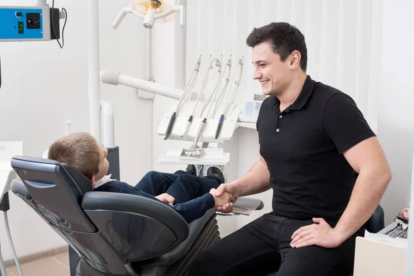 Odontólogo pediátrico estrechando la mano con un paciente joven en el consultorio dental. Odontología. Equipos dentales —  Fotos de Stock