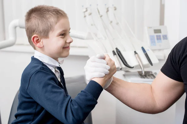 El dentista pediátrico da la mano a un niño pequeño, felicita al paciente por una operación exitosa en el consultorio dental. Odontología. Equipos dentales — Foto de Stock