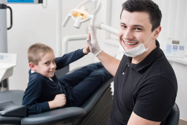 Παιδοδοντίατρος χειραψία με νεαρό αγόρι, να συγχαρώ την ασθενή για την επιτυχή λειτουργία στο οδοντιατρείο. Οδοντιατρική. Οδοντιατρικός εξοπλισμός — Φωτογραφία Αρχείου