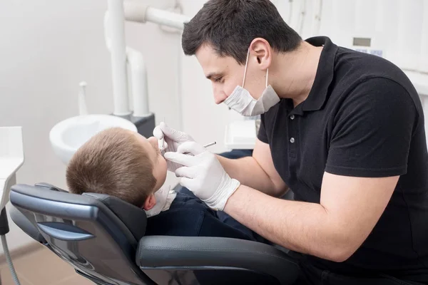 Pediatric tandläkare undersöker tänder av pojken patient i tandvårdsklinik med dental verktyg - spegel och sond. Tandvård — Stockfoto