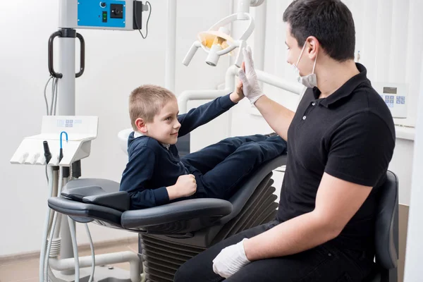 Kinderzahnarzt gibt High Five kleinen Jungen, gratulieren Patienten für eine erfolgreiche Operation in der Zahnarztpraxis. Zahnmedizin. Zahnmedizinische Geräte — Stockfoto