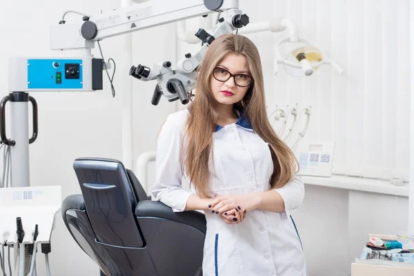 Πορτρέτο του όμορφη γυναίκα οδοντίατρος με μικροσκόπιο στο σύγχρονο οδοντιατρείο. Ο γιατρός φοράει γυαλιά, λευκή στολή. Οδοντιατρική — Φωτογραφία Αρχείου
