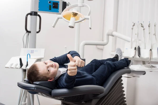 Happy patient boy showing thumbs up at dental office. Medicine, stomatology and health care concept. Dental equipment Royalty Free Stock Photos