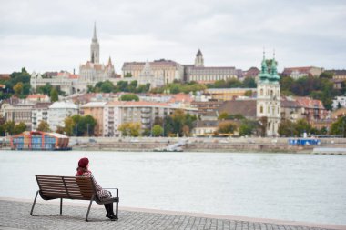 Kırmızı bere kız Budapeşte Nehri yakınında çıkabilir ve Buda yan Budapeşte Buda Castle, St. Matthias ve Fisherman's Bastion görünümünü bir bankta oturur. Arka plan bulanık. Arkadan Görünüm