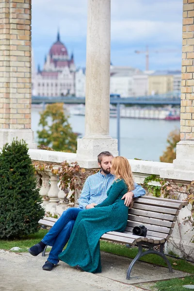 Young couple kissing on bench near columns on blurred background of Budapest architecture