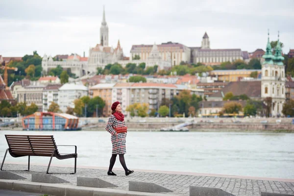 A stylish girl walks along the embankment of Budapest with blurred view of Buda side of Budapest with the Buda Castle, St. Matthias and Fisherman 's Bastion — стоковое фото