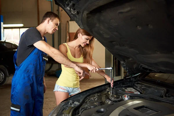 Mecánico muestra a una joven hembra cómo utilizar una llave inglesa para reparar un coche —  Fotos de Stock