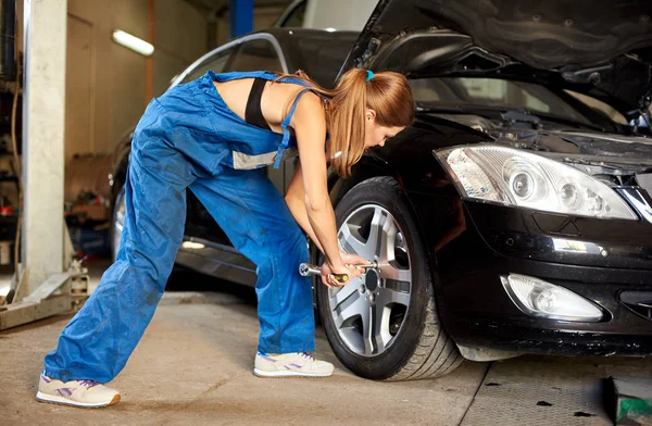 Young female professional repairing the black car and tightening the tire bolt. Royalty Free Stock Images