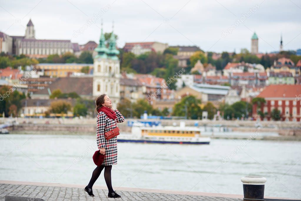 Tender woman enjoys lonely embankment of Budapest with blurred view of Buda side of Budapest with the Buda Castle, St. Matthias and Fisherman's Bastion.