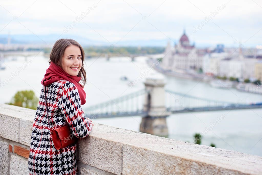 Close-up of a nice female looking back at the camera with smile against beautiful view of the Hungarian Parliament and the chain bridge in Budapest, Hungary. Blurred background